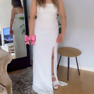 Vit långklänning från Club L London - Säljer en elegant vit långklänning från Club L London. Klänningen är axelbandslös med figurnära passform och har en hög slits framtill. Perfekt för bal eller festliga tillfällen. Materialet känns mjukt och följsamt.