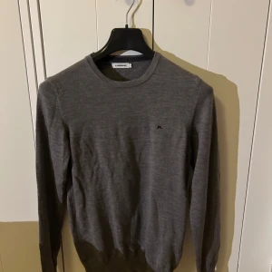 J.Lindberg tröja  - Säljer en stilren grå tröja från J.Lindeberg i 100% merinoull. Tröjan har rund halsringning och långa ärmar, perfekt för lager-på-lager eller som den är. Enkel och klassisk design med liten logga på bröstet.