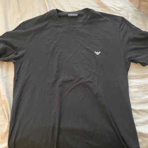 Svart t-shirt från Emporio Armani - Säljer en stilren svart t-shirt från Emporio Armani med liten logga på bröstet. Klassisk passform och rund halsringning. Perfekt för dig som gillar enkla och snygga plagg med exklusiv känsla. Helt ny ny pris 1000