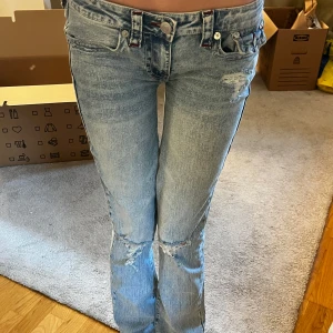 True Religion jeans low waist bootcut ”Becca” - Säljer ett par ljusblå bootcut jeans från True Religion med hål på knä och lår. Jeansen har klassiska bakfickor med broderad logga och silverfärgade knappar 💕 Modellen heter ”Becca” och de är egentligen mid waist men jag har sytt om de till lågmidjade!!! Jag är 167cm och storleken är 27 på jeansen ❤️(aldrig använt) köpta för 1299kr på Nelly 