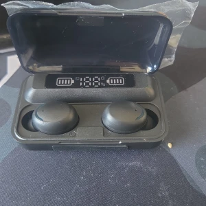 Svarta trådlösa hörlurar med laddningsetui - Säljer ett par svarta trådlösa hörlurar med digital display på laddningsetuiet som visar batterinivå. Etuiet har både USB och USB-C port för laddning. Perfekt för musik och samtal på språng.