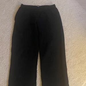 Svarta mjukisbyxor med rak passform - Svarta mjukisbyxor med elastisk midja och rak, loose passform. Perfekta för en avslappnad stil och sköna att ha på sig hela dagen. Byxorna är tillverkade i mjukt material och har en enkel, stilren look.