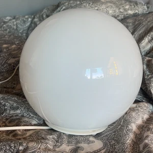 vit rund bordslampa - Säljer en rund bordslampa från IKEA, modell FADO. Lampan är helt vit och har en klotformad design i glas med vit sladd och strömbrytare. Perfekt som mysbelysning i sovrum eller vardagsrum. Bra ljus och den är i möjlighet att byta glödlampa ifall någon vill det. USB uttag. 