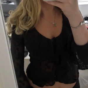 Svart spetsblus med knappar - Säljer en svart, transparent blus i spets med långa ärmar och knappar framtill. Perfekt för dig som vill ha en trendig och elegant topp till din garderob.