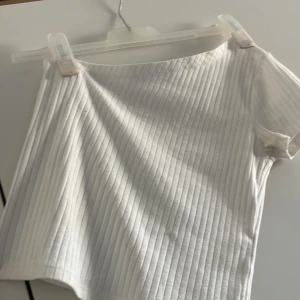 Vit ribbad one shoulder topp - Säljer en vit ribbad topp med one shoulder-design. Toppen har en tight passform och är tillverkad i ett mjukt, stretchigt material. Perfekt för att skapa en trendig och stilren look.