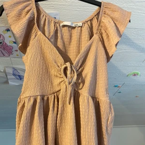 Rosa/beige blus med volangärm från 157 - Supersöt rosa/beige blus från 157 med volangärmar och knyt framtill. Tillverkad i ett mjukt, strukturerat material som ger en avslappnad känsla. 