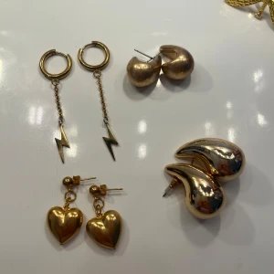 Mix av guldiga örhängen - Säljer fyra par guldiga örhängen: ett par med blixtar på kedja, ett par hjärtformade, ett par chunky halvmåneformade och ett par runda klot. Perfekta och så fina, 49kr/st💖💖