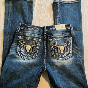 Blå bootcut från Miss Me  - Säljer ett par blå jeansbyxor från Miss Me med snygga broderade detaljer och dekorationer på bakfickorna. Jeansen har normal passform och klassisk femficksdesign med kontrastsömmar. Pris kan diskuteras