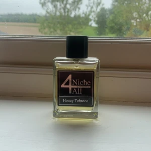 Honey Tobacco parfym från 4Niche All - En elegant parfymflaska i glas med svart lock från 4Niche All. Doften heter Honey Tobacco och kombinerar söta och rökiga toner. Flaskan är rektangulär och transparent med en stilren etikett i svart och guld. Väldigt lik naxos ca 95ml kvar