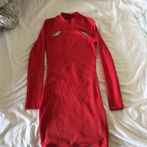 Röd ribbad långärmad klänning med cut-outs - Säljer en tight röd ribbad klänning med långa ärmar och coola cut-outs vid axlarna. Klänningen har en hög hals och är i stretchigt material som sitter snyggt på kroppen. Perfekt för dig som vill sticka ut!