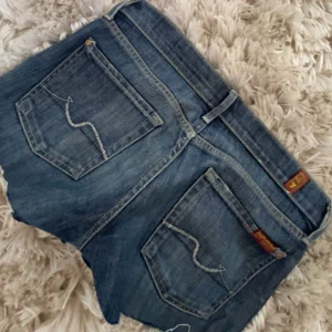 Jeansshorts från 7 For All Mankind - Snygga blå jeansshorts från 7 For All Mankind med råa kanter och klassiska bakfickor. Modellen är lågmidjad och har knapp- och dragkedjestängning. Perfekta för sommaren!