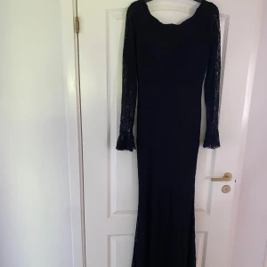 Svart långklänning med spetsärmar - Elegant svart långklänning med figurnära passform och långa spetsärmar. Klänningen har en djup rygg med dragkedja och vackra spetsdetaljer vid ärmsluten. Perfekt för en kväll när du vill känna dig extra snygg. Storleken är M men passar även för S.