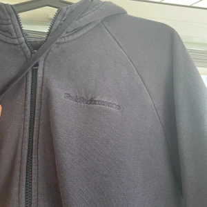 Svart hoodie från Peak Performance - Säljer en marinblå hoodie från Peak Performance med dragkedja framtill och huva med dragsko. Tröjan har två fickor på magen och diskret broderad logga på bröstet. 
