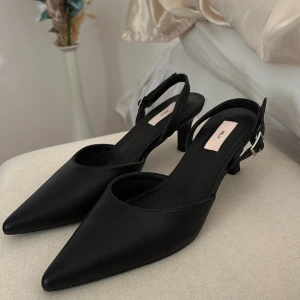 Svarta pumps med klack och spetsig tå - Säljer ett par eleganta svarta pumps från Nelly med spetsig tå och smal klack. Skorna har en justerbar rem med silverfärgat spänne runt hälen. Perfekta för dig som gillar stilrena och klassiska skor. Använt de kanske 2-3 gånger men har inga defekter, super sköna och fina!🥰