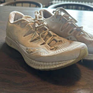 Vita löparskor från Saucony - Säljer ett par vita löparskor från Saucony med snygg mesh-överdel och reflekterande detaljer. Skorna har snörning och en bekväm, dämpad sula som passar perfekt för löpning eller träning. Lätta och ventilerande för bästa komfort.