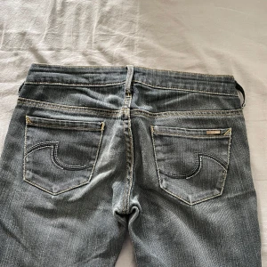 lågmidjade jeans - Säljer ett par grå jeansbyxor med snygga kontrastsömmar och klassiska fickor. Byxorna har låg midja och raka ben. Perfekta för dig som gillar en enkel men stilren look.