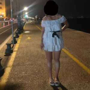 Vit prickig offshoulder klänning med volanger - Söt vit kortklänning med svarta prickar och volanger. Offshoulder-modell med resår upptill och ett svart knytband i midjan. Klänningen har flera lager volanger och är luftig, perfekt för varma dagar.