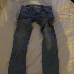 Ljusblå jeansbyxor från Nudie Jeans - Säljer ett par ljusblå jeansbyxor från Nudie Jeans med klassisk femficksdesign och raka ben. Jeansen har normal passform och är tillverkade i denim med snygga detaljer på bakfickorna.
