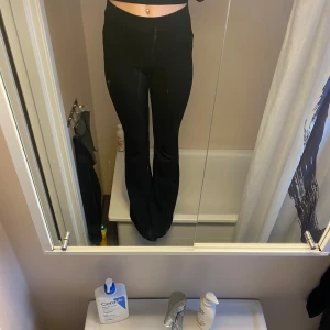 Svarta bootcut byxor med dragsko - Svarta byxor med bootcut-stil och dragsko i midjan. Mjukt material och hög midja, perfekta för en avslappnad och trendig look. Passar bra till crop tops eller hoodies. Fläckarna är på spegeln och inte byxorna! Man kan vika ner dem så de blir low waist själv tycker jag det blir snyggare.