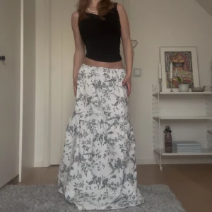 Vit långkjol med blommigt mönster - Säljer en vit långkjol med svart blommigt mönster. Kjolen är iav bummul med resår i midjan. Superfin till sommaren! Ställ gärna frågor och pris kan diskuteras🩷🌸
