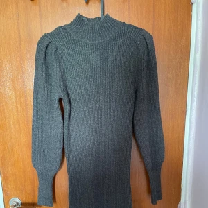 Mörkgrå ribbad stickad långklänning från ONLY - Säljer en mörkgrå stickad långklänning från ONLY med ribbad struktur. Klänningen har långa ärmar med lätt puff vid axlarna och en hög hals. Perfekt för kyligare dagar och enkel att styla med boots eller sneakers.