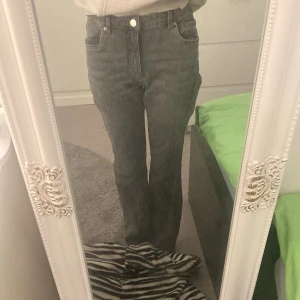 Grå bootcut jeans - Säljer ett par gråa bootcut jeans med hög midja. Jeansen har klassiska fem fickor och stängs med knapp och dragkedja. Perfekta för dig som gillar en tidlös och avslappnad stil.