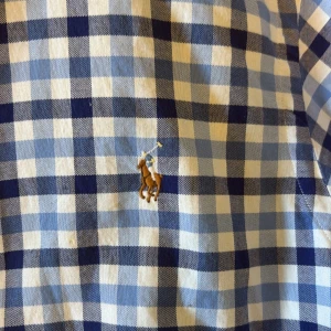 Blårutig skjorta från Ralph Lauren - Säljer en klassisk blårutig skjorta från Ralph Lauren i slim fit-modell. Skjortan har knappar framtill, button-down krage och den ikoniska broderade loggan på bröstet. Perfekt för dig som gillar stilrena och tidlösa plagg.