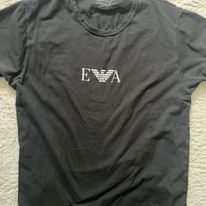 Svart t-shirt från Emporio Armani - Säljer en svart t-shirt från Emporio Armani med logga i vitt framtill. Klassisk rund halsringning och korta ärmar. Perfekt för en stilren och enkel look.