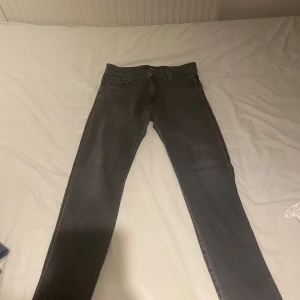 Grå jeansbyxor Replay Anbass - Säljer ett par grå Replay Anbass jeans med klassisk femficksdesign och dragkedja. Byxorna har en slim passform och raka ben. Perfekta för dig som gillar stilrena och bekväma jeans. Buda gärna! FÖRST TILL KVARN!
