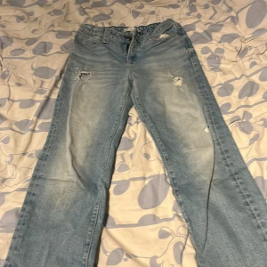 Ljusblå slitna jeans från Tommy Hilfiger - Säljer ett par ljusblå jeans från Tommy Hilfiger med slitna detaljer och hål på framsidan. Jeansen har klassisk femficksdesign, knappgylf och raka ben. Perfekta för en avslappnad stil.
