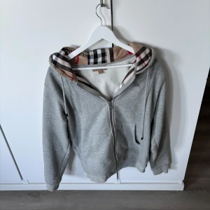 Grå Burberry zip hoodie - Tjena! Säljer en grå hoodie från Burberry med dragkedja och klassiskt rutigt foder i huvan. Snyggaste tröjan till vår/sommarkvällar.