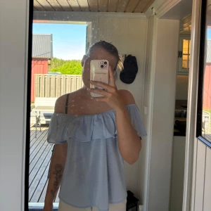 Ljusblå offshoulder blus - Säljer en ljusblå blus med offshoulder och volangdetalj upptill. Blusen har en luftig passform och är perfekt för varma dagar. Superfin att styla med både jeans och kjol!