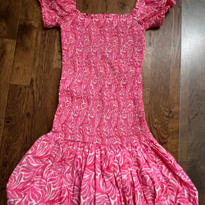 Rosa kortklänning med puffärmar - Söt rosa kortklänning med vitt bladmönster och smockad överdel. Klänningen har puffiga kortärmar och en volangig kjol. Perfekt för sommarens alla tillfällen! Från HM och säljs ej längre💗Använd en gång!