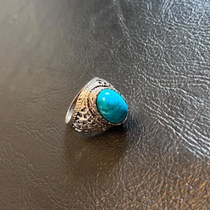 Silverring med turkos sten - Storlek:19,8mm-20mmCool silverfärgad ring med en stor oval turkos sten i mitten. Ringen har ett detaljerat, nästan antikt mönster runt stenen och sidorna är utskurna med snygga detaljer. Perfekt statement-piece för dig som vill sticka ut.