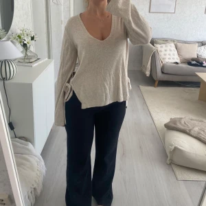 Beige v-ringad tröja med knyt från Lindex - Säljer en beige v-ringad tröja från Lindex i mjuk stickad kvalitet. Tröjan har långa ärmar och snygga knytband i sidorna som ger en chill och trendig vibe. Passformen är normal och materialet känns skönt mot huden. Perfekt för dig som gillar enkla men stilrena plagg.