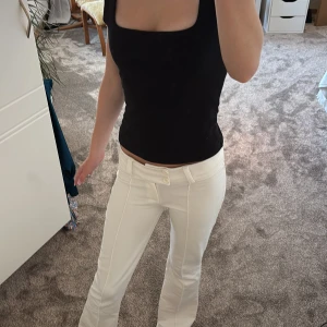 Vita bootcut byxor med låg midja - Säljer ett par vita bootcut byxor med låg midja och snygga sömmar framtill. Byxorna har två knappar i midjan och bälteshällor. Materialet känns mjukt och stretchigt. Passformen är slim upptill och lite utsvängd nedtill.