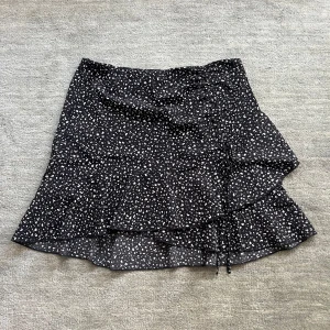 Svart volangkjol med vitt mönster - Säljer nu denna svartvita volangkjol med en osynlig dragkedja och ett fint resorband som man kan knyta till en rosett längst ner eller dra åt som syns på bilden! Köpt för 120 kr men säljer nu för 49 kr! Använd endast ett fåtal gånger!💗💗