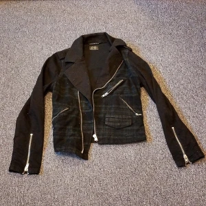 Svart bomberjacka från D-ID - Snygg svart bomberjacka från D-ID med croppad passform och coola dragkedjor på ärmar och framtill. Jackan har ett diskret rutigt mönster och flera fickor med dragkedja. Perfekt för dig som gillar en edgy stil och vill sticka ut. Tvättas innan jag skickar det om du vill😄