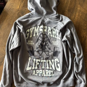 Grå Gymshark hoodie med tryck - Säljer en grå/blå hoodie från Gymshark med gym bunny print på ryggen, nästan aldrig använd då den va för stor för mig, jätteskönt material verkligen!