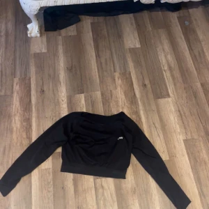 Svart croppad tröja från ICANIWILL - Säljer en svart croppad långärmad tröja från ICANIWILL. Tröjan har en stilren design med diskret logga på bröstet och bred mudd nedtill. Materialet är mjukt och stretchigt med 92% nylon och 8% spandex, perfekt för träning eller chill.