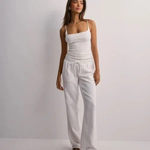 Vita linnebyxor med snörning - Säljer ett par fräscha vita linnebyxor med avslappnad passform och snörning i midjan. Byxorna har raka ben, två stora fickor fram och är tillverkade i mjukt linne som känns svalt och skönt. Lågmidjade