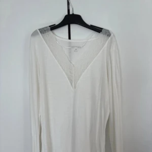 Vit långärmad blus med spets från Stories - Säljer en vit långärmad blus från Stories i storlek M. Toppen har en djup v-ringning med transparent spetsdetalj vid halsen som ger en extra touch. Materialet känns lätt och mjukt, perfekt för dig som gillar stilrena och feminina plagg.