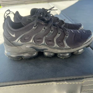 Nike Air Vapormax Plus svarta sneakers - Svarta Nike Air Vapormax Plus sneakers med chunky, genomskinlig sula och coolt mönstrad ovandel i syntet. Snygga detaljer med snörning och diskret Swoosh på sidan. Perfekt för dig som gillar streetstyle och vill ha en unik look. PRIS KAN DISKUTERAS 