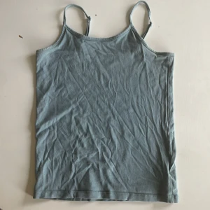 Blå linnetopp från 157 med smala axelband - Snygg blå linnetopp från 157 med smala justerbara axelband. Toppen är enkel och stilren, perfekt att matcha med jeans eller shorts. Materialet är mjuk bomull med lite stretch för extra komfort. Passformen är normal och toppen är ärmlös.