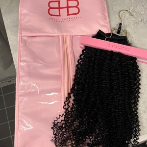Hello Bombshell hårförlängning (clips) - Säljer hårförlängning från Hello Bombshell! Håret har färgen 1B (natural black) och lockigt.   Längd: 53cm  Vikt: 130 gram  Håret är oanvänt, i och med att förseglingen var bruten så gick det inte att returnera.   Kommer i tillhörande förvaringspåse!🩷  Ordpris 1.799