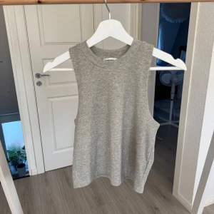 Grå ribbad linnetopp - Snygg glittrig grå linnetopp med breda axelband och ribbad struktur. Modellen är ärmlös och har en rundad halsringning. Toppen är helt oanvänd. 