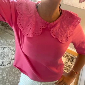 Rosa topp med broderad krage - Säljer en söt rosa topp med broderad krage i spets och blommönster. Toppen har halvlånga ärmar och är gjord i mjukt bomullsmaterial💝Perfekt för dig som vill sticka ut med en färgglad och söt detalj! Den är använd 1 gång. Storleken är M men skulle passa S också