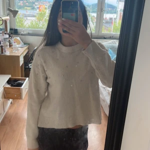 Vit stickad tröja med pärlor från H&M - Säljer en vit stickad tröja från H&M i storlek XS. Tröjan har långa ärmar och är dekorerad med små pärlor över hela framsidan och ärmarna. Den har en rund hals och breda ribbade muddar vid ärmslut och nederkant. Perfekt för dig som gillar stilrena detaljer.