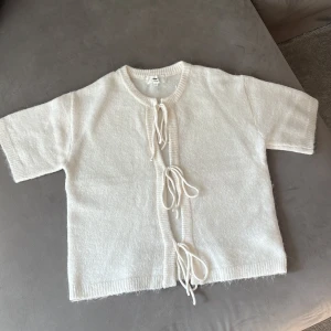 Vit kofta med snörning från Gina Tricot - Superfin vit kofta från Gina Tricot i mjuk ullblandning. Kortärmad modell med rund hals och snörning framtill som ger en chill vibe. Perfekt att slänga över en topp för extra lager. Ribbstickade kanter och loose fit för skön känsla.