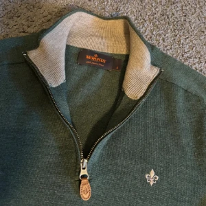  Morris half zip - Snygg grön tröja från Morris i 100% merinoull med half zip och ribbad beige krage. Liten broderad logga på bröstet och långa ärmar. Perfekt för dig som gillar stilrena och klassiska plagg med en modern touch. OBS tröjan är en liten s model så om du har xs är den nog perfekt för dig 